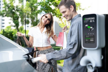 Photo for Young couple travel with EV electric car charging in green sustainable city outdoor garden in summer shows urban sustainability lifestyle by green clean rechargeable energy of electric vehicle innards - Royalty Free Image