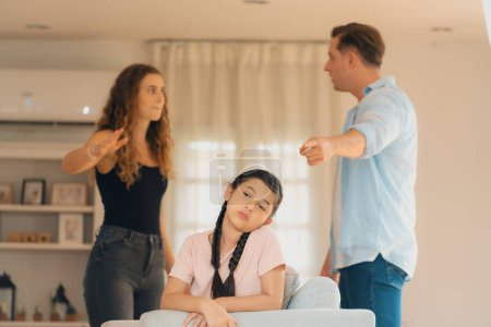 Photo for Annoyed and unhappy young girl sitting on sofa trapped in middle of tension by her parent argument in living room. Unhealthy domestic lifestyle and traumatic childhood develop to depression.Synchronos - Royalty Free Image
