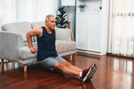 Foto de Hombre mayor atlético y activo que utiliza muebles para dirigir el músculo eficaz con empuje hacia arriba en el ejercicio en el hogar como concepto de estilo de vida corporal en forma saludable después de la jubilación. Clout. - Imagen libre de derechos