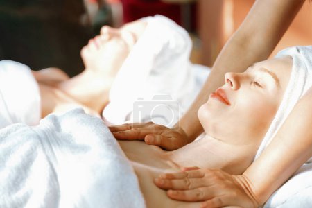 Foto de Un retrato de dos hermosas mujeres teniendo masaje de espalda por masajista profesional y cayendo en profunda relajación rodeada de un ambiente de spa tradicional. Concepto calmante y relajante. Tranquilidad. - Imagen libre de derechos
