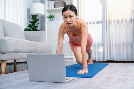 Photo for Asian woman in sportswear doing burpee on exercising mat as home workout training routine. Attractive girl engage in her pursuit of healthy lifestyle with online exercise training video. Vigorous - Royalty Free Image