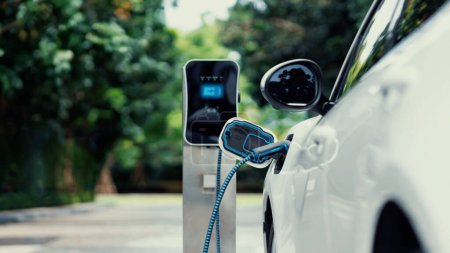 Photo for Electric car plugged in with charging station to recharge battery with electricity by EV charger cable in eco green park and greenery foliage. Future innovative ev car and energy sustainability.Peruse - Royalty Free Image