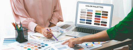 Photo for Creative graphic design presents selective color while manager using laptop comparing suitable color at table with color palettes, graphic material scatter around at modern office. Variegated. - Royalty Free Image