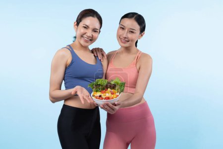 Téléchargez les photos : Deux jeunes femmes asiatiques sportives en tenue de sport tenant saladier remplissent de fruits et légumes. Naturel jeune et en forme mode de vie des gens avec équilibre nutritionnel sur fond isolé. Vigoureux - en image libre de droit