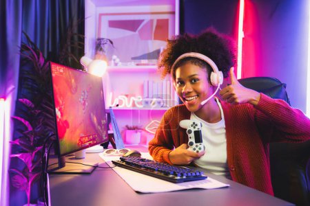 Photo for African American girl gaming streamer team winner playing online fighting with Esport wearing headphones in neon lighting room. Talking other players planing strategies to win competitors. Tastemaker. - Royalty Free Image