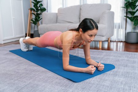 Foto de Ajuste joven mujer asiática cepillando en el piso de la sala de estar. Rutina de entrenamiento de estilo de vida saludable en casa. Equilibrio y resistencia ejerciendo el concepto. Vigoroso - Imagen libre de derechos