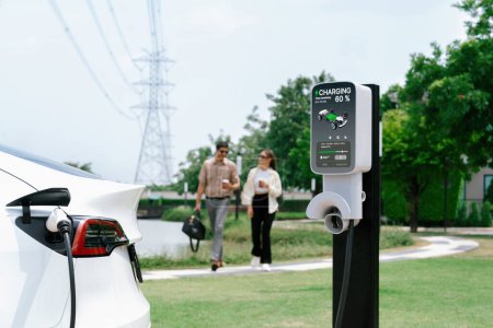 Photo for Young couple with coffee recharge EV car battery at charging station connected to electrical industrial power grid tower. Couple with shopping and travel using eco electric car lifestyle. Expedient - Royalty Free Image