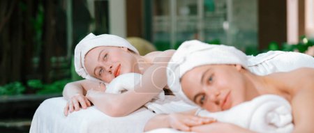 Téléchargez les photos : Un portrait d'un couple d'une belle jeune femme caucasienne avec serviette blanche repose sur un lit de spa confortable avec détente tout en ayant massage du corps avec masseur professionnel au salon de spa.. - en image libre de droit