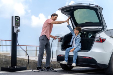 Photo for Family road trip vacation traveling by the sea with electric car, father and son high five after reach destination at EV charging station by the seashore. Eco-friendly car for environment. Perpetual - Royalty Free Image