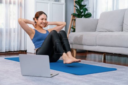 Photo for Asian woman in sportswear doing crunch on exercising mat as home workout training routine. Attractive girl engage in her pursuit of healthy lifestyle with online exercise training video. Vigorous - Royalty Free Image