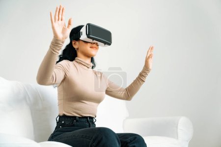 Téléchargez les photos : Jeune femme utilisant réalité virtuelle VR masque à la maison pour une expérience d'achat en ligne cruciale. L'innovation VR en réalité virtuelle optimisée pour le divertissement numérique féminin. - en image libre de droit