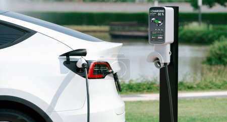 Téléchargez les photos : Batterie de recharge de voiture électrique EV au parking dans le parc vert de la ville. Technologie d'énergie propre alternative pour une automobile rechargeable pour des déplacements urbains durables et respectueux de l'environnement. Expedient - en image libre de droit