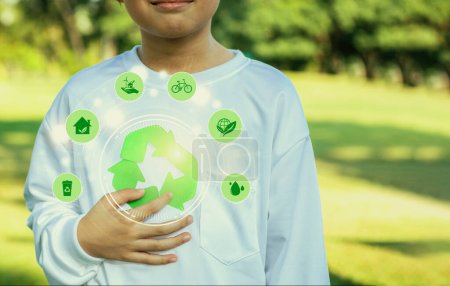 Téléchargez les photos : Symbole de recyclage vert pour la durabilité environnementale et la campagne de sensibilisation à la protection naturelle avec un petit garçon flou promouvant les pratiques ESG recyclables à l'arrière-plan du parc extérieur. Dépendance - en image libre de droit