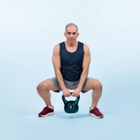 Photo for Full body length shot athletic and sporty senior man doing squat with kettlebell for body workout on isolated background. Healthy active physique and body care lifestyle after retirement. Clout - Royalty Free Image