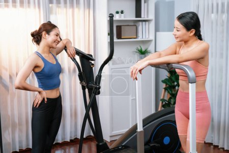 Photo for Energetic and strong athletic asian woman running on elliptical running machine at home with workout buddy or trainer. Pursuit of fit physique and commitment to healthy lifestyle. Vigorous - Royalty Free Image