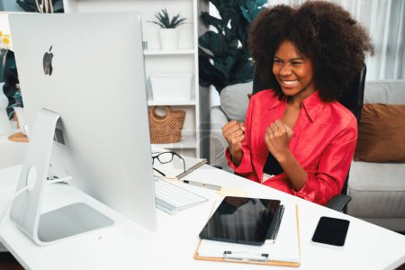Téléchargez les photos : Une blogueuse africaine est sortie avec un visage heureux, regardant à l'écran avec une réalisation boursière appréciée à un profit élevé. Concept d'investissement en bourse en ligne dans l'application de trading sur pc. Tastemaker. - en image libre de droit