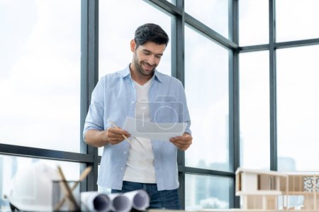 Photo for Expert civil engineer holding blueprint while comparing with house model on table with architectural equipment, document,blueprint house model scatter around. Real estate design concept. Tracery. - Royalty Free Image