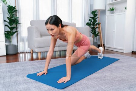 Photo for Asian woman in sportswear doing burpee on exercising mat as home workout training routine. Attractive girl engage in her pursuit of healthy lifestyle and fit body physique. Vigorous - Royalty Free Image