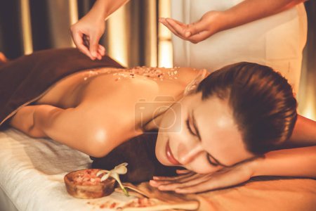 Photo for Woman customer having exfoliation treatment in luxury spa salon with warmth candle light ambient. Salt scrub beauty treatment in Health spa body scrub. Quiescent - Royalty Free Image