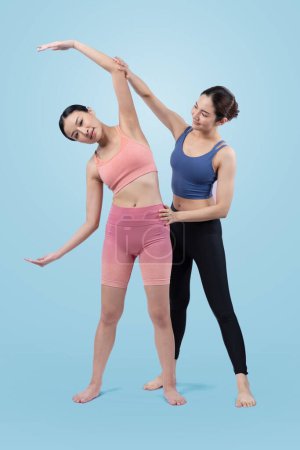 Photo for Asian woman in sportswear doing yoga exercise in standing pose with her trainer or yoga buddy. Healthy body care and meditation yoga lifestyle in full shot on isolated background. Vigorous - Royalty Free Image