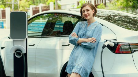 Photo for Beautiful young woman recharging her electric car from home EV charging station using alternative energy with net zero emission. Modern young girl charging her vehicle before vacation travel.Perpetual - Royalty Free Image