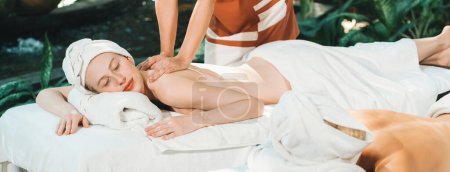 Téléchargez les photos : Couple de belle jeune femme allongée sur un lit de spa blanc pendant le massage du dos. Belle femme caucasienne ayant massage du dos à la salle de spa traditionnelle. Concept relaxant et sain Tranquillité. - en image libre de droit