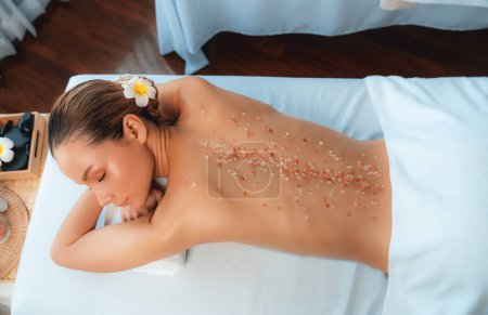 Photo for Panorama top view woman customer having exfoliation treatment in luxury spa salon with warmth candle light ambient. Salt scrub beauty treatment in health spa body scrub. Quiescent - Royalty Free Image