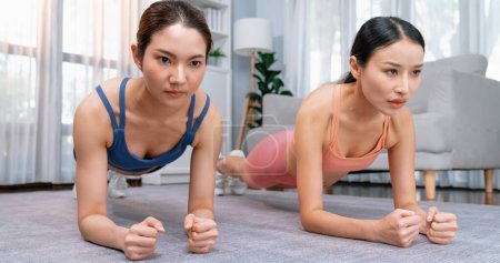Foto de Ajuste joven mujer asiática cepillando en el piso de la sala de estar con su entrenador o compañero de ejercicio. Rutina de entrenamiento de estilo de vida saludable en casa. Equilibrio y resistencia ejerciendo el concepto. Vigoroso - Imagen libre de derechos
