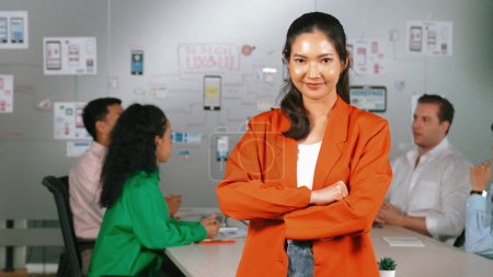 Téléchargez les photos : Femme d'affaires professionnelle asiatique debout avec confiance lors d'une réunion d'affaires créative. Belle leader confiant posant tandis que les gens d'affaires divers discussion sur l'utilisation Ux et Ui design - en image libre de droit