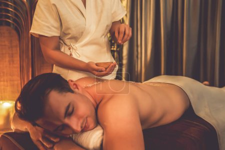 Photo for Man customer having exfoliation treatment in luxury spa salon with warmth candle light ambient. Salt scrub beauty treatment in Health spa body scrub. Quiescent - Royalty Free Image