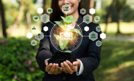 Téléchargez les photos : Une jeune plante concentrée sur le sol avec ESG et une icône écologique tenue par une femme d'affaires floue symbolisent la protection de l'environnement et la préservation de la nature pour un avenir plus vert. Dépendance - en image libre de droit