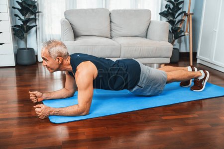 Téléchargez les photos : Athlétique et sportif homme âgé planches sur tapis d'exercice de remise en forme à la maison exercice comme concept de mode de vie de corps en bonne santé après la retraite. Clout - en image libre de droit