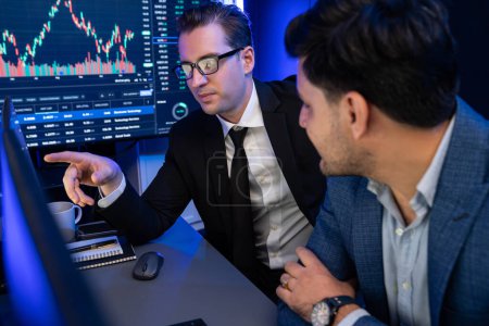 Photo for Two stock exchange traders discussing dynamic investment graph in currency rate on monitor at night. Businessman partners coffee meeting in high stock market in neon light at workplace. Sellable. - Royalty Free Image