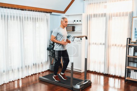 Photo for Active senior man running on tread running machine at home together in full body shot as fitness healthy lifestyle and body care after retirement for pensioner. Clout - Royalty Free Image