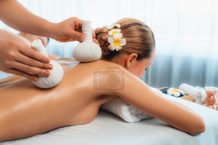 Photo for Hot herbal ball spa massage body treatment, masseur gently compresses herb bag on couple customer body. Tranquil and serenity of aromatherapy recreation in day lighting ambient at spa salon. Quiescent - Royalty Free Image