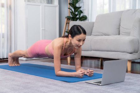 Photo for Fit young asian woman planing on the living room floor while following exercise instruction on online training video. Healthy lifestyle workout routine at home. Balance and endurance concept. Vigorous - Royalty Free Image