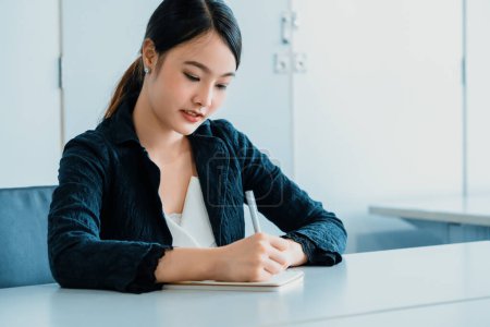Photo for Beautiful young Asian woman writes letter on notebook while sitting at office desk. Content writer and secretary job concept. uds - Royalty Free Image