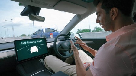 Téléchargez les photos : Voiture autonome ou véhicule autonome se déplacent sur l'autoroute de la vitesse avec le système sans conducteur et le mode pilote automatique permettant à l'homme conducteur se détendre et se concentrer sur smartphone sans compromettre la sécurité. Perpétuel - en image libre de droit