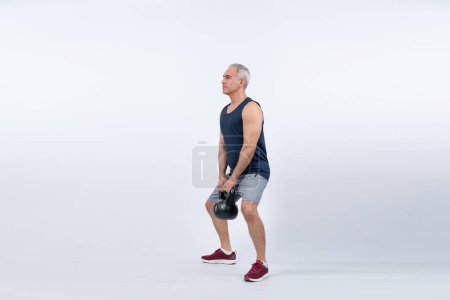 Téléchargez les photos : Pleine longueur du corps tourné sportif et sportif senior homme faisant squat avec kettlebell pour l'entraînement du corps sur fond isolé. Mode de vie sain et actif après la retraite. Clout - en image libre de droit