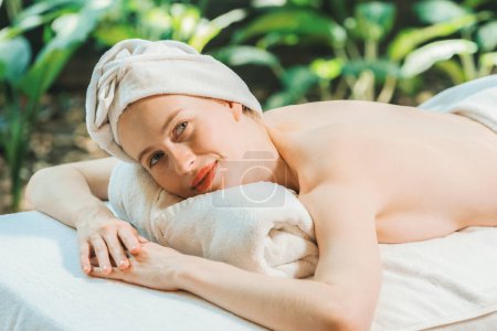 Photo for A beautiful young woman lies on a spa bed while looking at camera. Feeling of relaxed and at peace. Attractive caucasian woman surrounded by the calming sounds of nature. Tranquility - Royalty Free Image