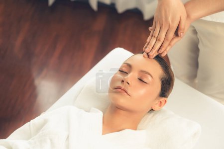 Téléchargez les photos : Femme caucasienne profiter relaxant anti-stress massage de la tête et choyer beauté du visage loisirs de la peau dans dayspa lumière moderne ambiant au complexe de luxe ou un salon de spa de l'hôtel. Tranquillité - en image libre de droit