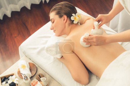 Photo for Hot herbal ball spa massage body treatment, masseur gently compresses herb bag on woman body. Tranquil and serenity of aromatherapy recreation in day lighting ambient at spa salon. Quiescent - Royalty Free Image