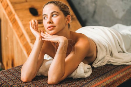 Photo for Pretty young woman lies on spa bed in front of wooden sauna cabinet. Attractive relaxing caucasian women in white towel waiting for body massage in spa salon, sauna room .Tranquility. - Royalty Free Image