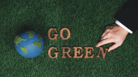 Photo for Message Go Green letter with planet Earth icon or symbol arranged by businessman hand to promote eco awareness as CSR effort for sustainable future with biophilc design background. Gyre - Royalty Free Image