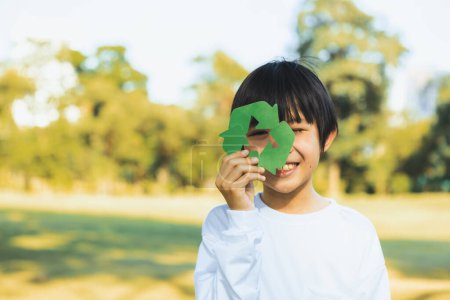 Téléchargez les photos : Joyeux jeune garçon asiatique tenant le symbole de recyclage sur le parc vert naturel de la lumière du jour promouvoir le recyclage des déchets, réduire et réutiliser les encouragements pour une sensibilisation éco durable pour les générations futures. Pneumatique - en image libre de droit
