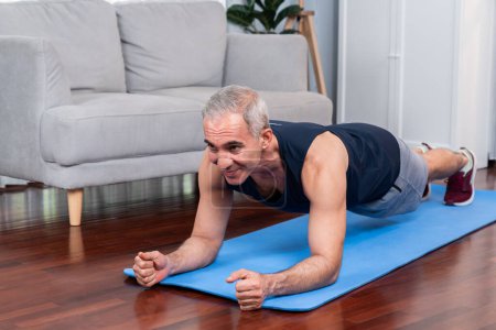 Téléchargez les photos : Athlétique et sportif homme âgé planches sur tapis d'exercice de remise en forme à la maison exercice comme concept de mode de vie de corps en bonne santé après la retraite. Clout - en image libre de droit