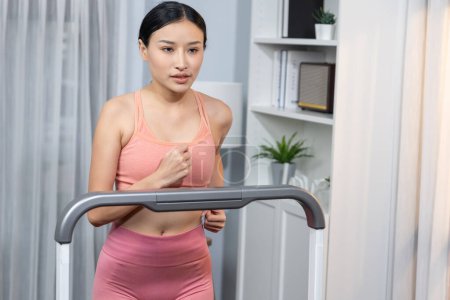 Téléchargez les photos : Energique et forte femme asiatique athlétique course machine à la maison. Poursuite de la forme physique et l'engagement à un mode de vie sain avec l'entraînement à domicile et la formation. Vigoureux - en image libre de droit