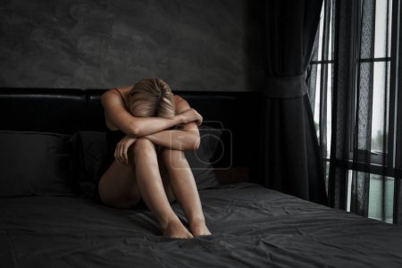 Photo for Young woman with critical depression and anxiety disorder from loneliness, mental sickness, or unwanted pregnancy, cuddling herself on dark bedroom. Overwhelming negative thought. Blithe - Royalty Free Image