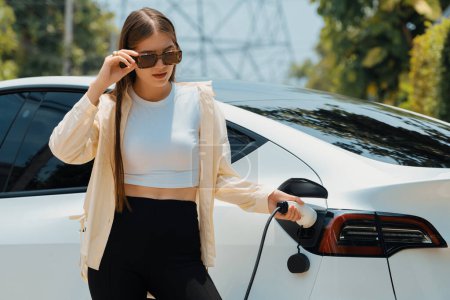 Photo for Young woman recharge her EV electric vehicle at green city park parking lot. Urban sustainability lifestyle for environmental friendly EV car with battery charging station. Expedient - Royalty Free Image