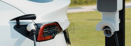 Téléchargez les photos : Closeup EV batterie de recharge de voiture électrique au parking dans le parc vert de la ville. Technologie alternative d'énergie propre pour une automobile rechargeable pour des déplacements urbains écologiques et durables. - en image libre de droit
